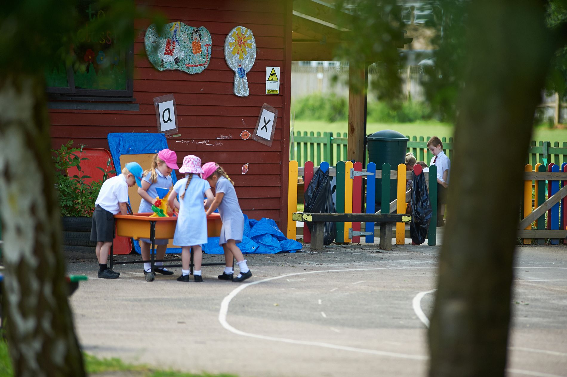 A small group of young pupils are pictured playing together outdoors with a sandpit.
