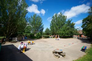 Wide shot of the outdoor play area at Paddock Wood Primary Academy. Some pupils are seen playing with one another.