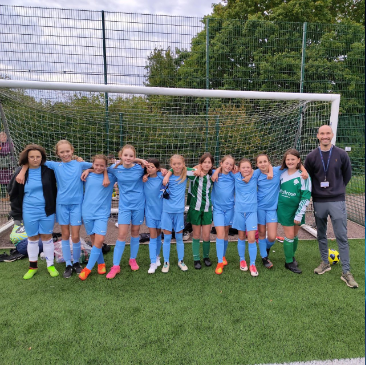 The Paddock Wood Primary Academy Girls' Football team are pictured posing together for a photo underneath a goalpost, alongside their teacher,
